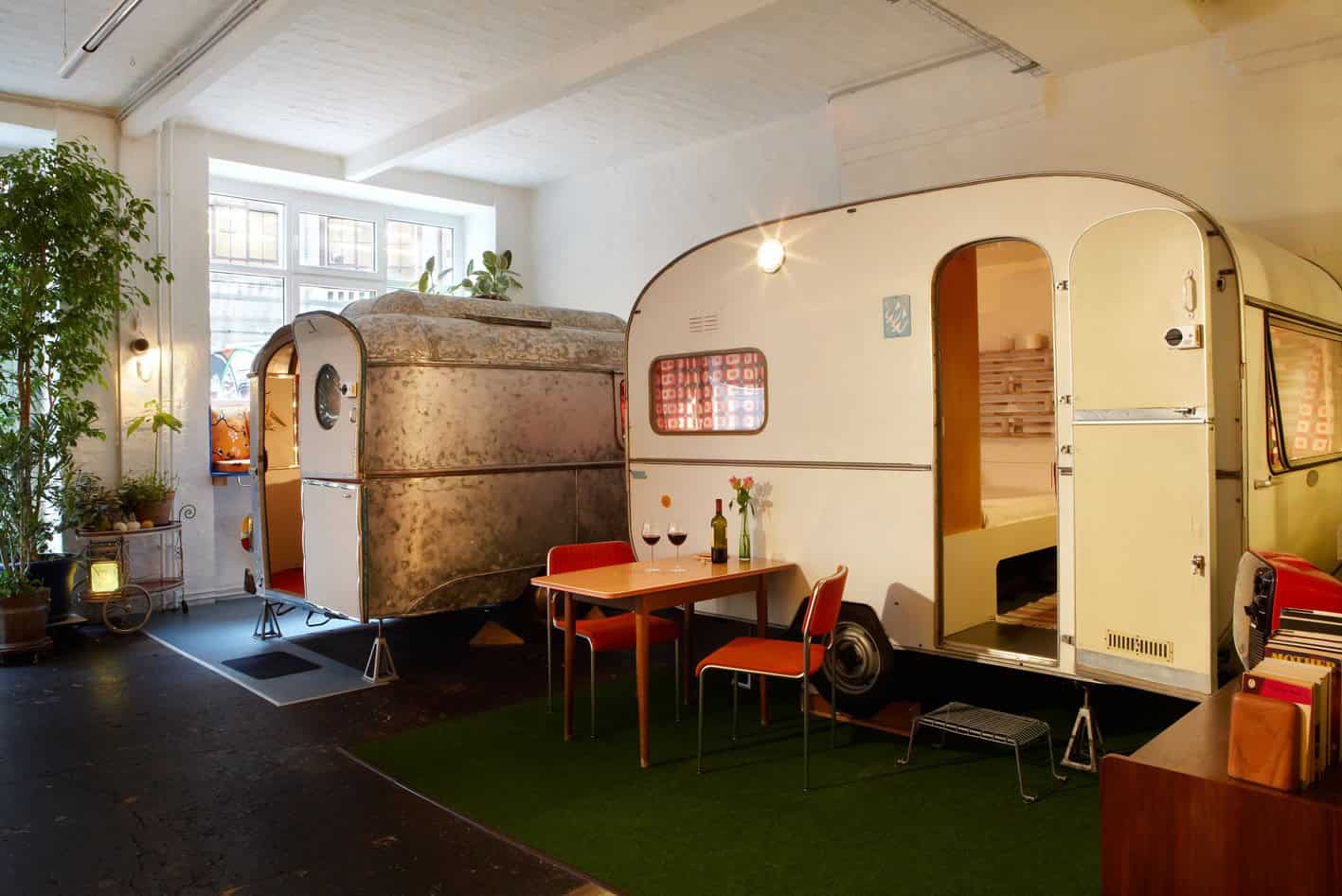 Two vintage caravans parked indoors with a small table on a patch of green carpet
