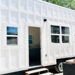 Bright white Noah-certified tiny house with large windows and outdoor seating.