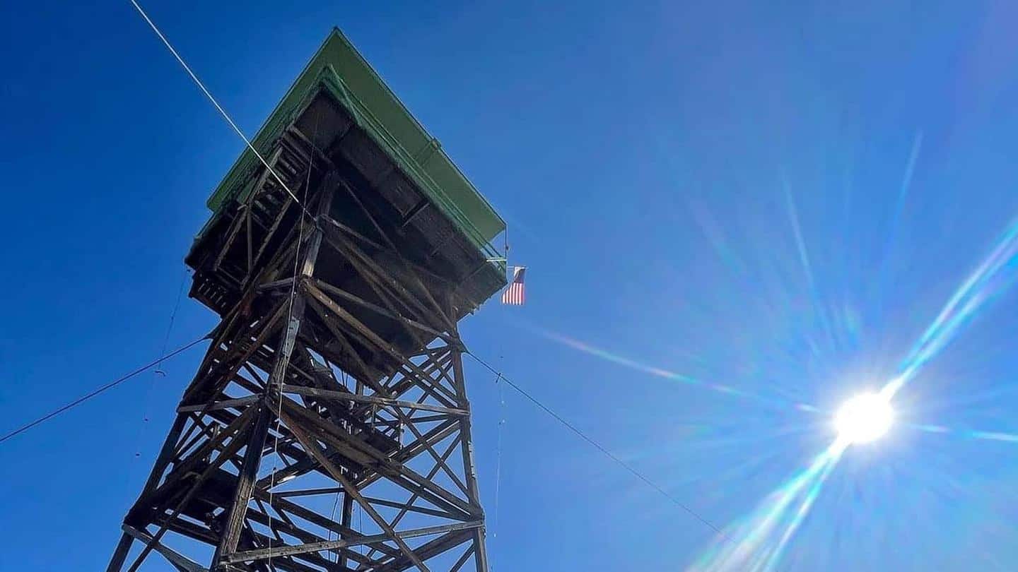 Low-angle view of Jersey Jim fire tower against blue sky with flag on the deck