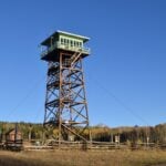 Jersey Jim Lookout: full timber fire tower with mint cab in an aspen-lined meadow, guy wires, autumn aspens