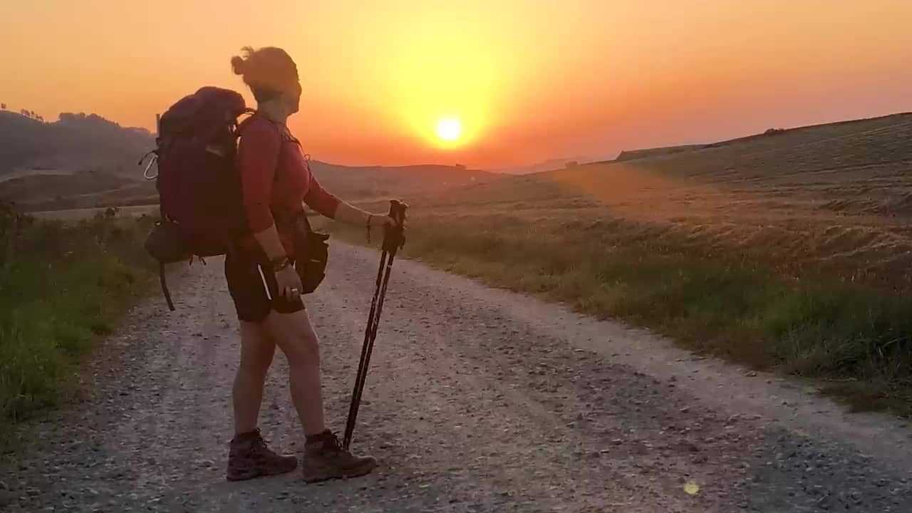 Joanne hiking a dirt road at sunset with a backpack and trekking pole on the Camino de Santiago