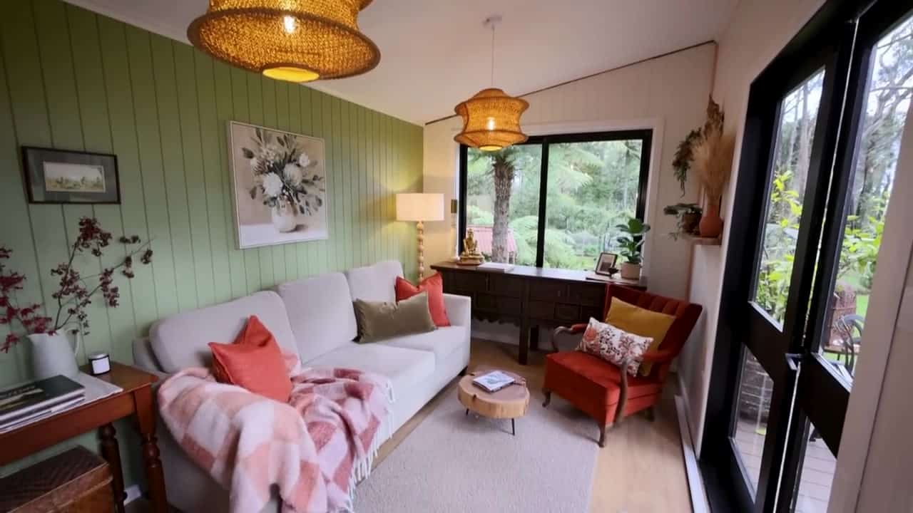 Separate living-pod lounge with a cream sofa, sage-green feature wall, rattan pendant lights, and a large window to Blue Mountains forest
