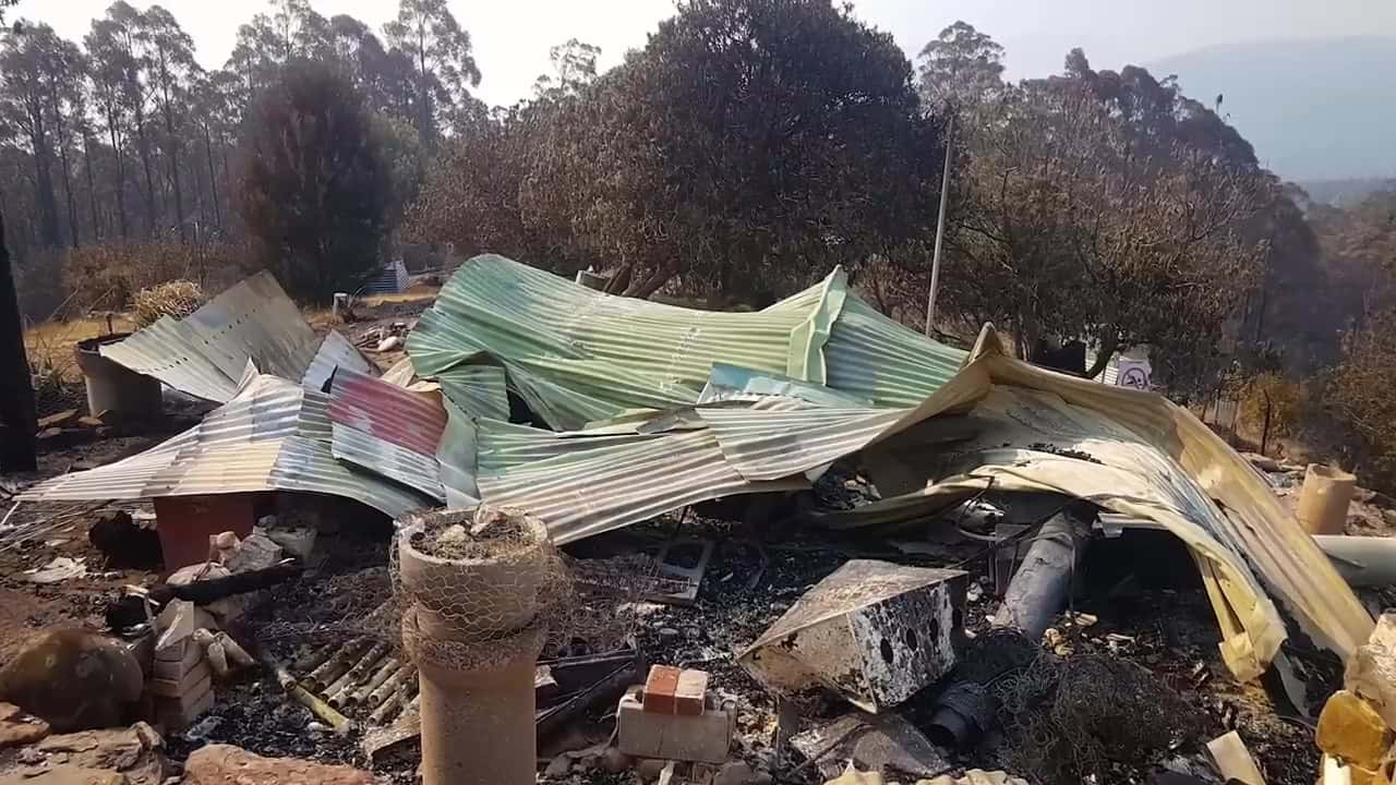 Twisted corrugated metal and ash where a building stood after a Tasmanian bushfire