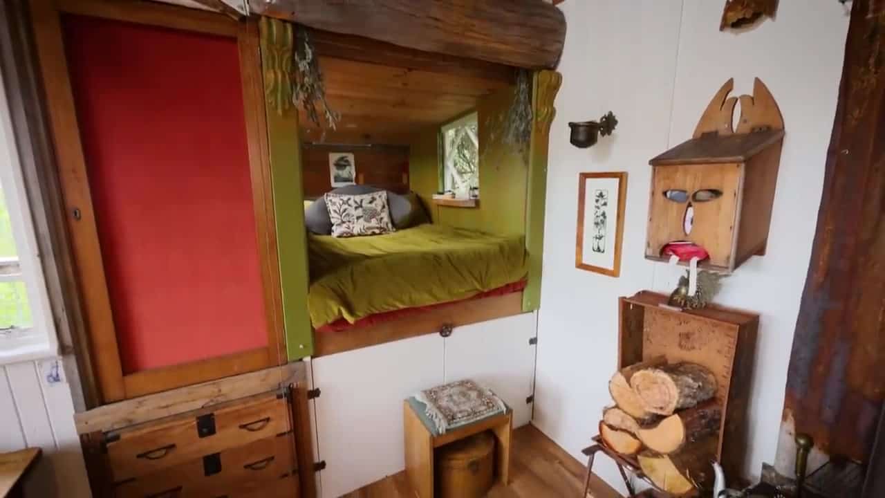 Bed nook pushed out of the cabin wall with olive bedding, a window to the trees, and storage cupboards underneath