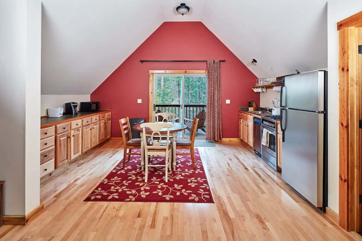 Kitchen with wood cabinets and stainless fridge leading to a round dining table by glass doors to the deck