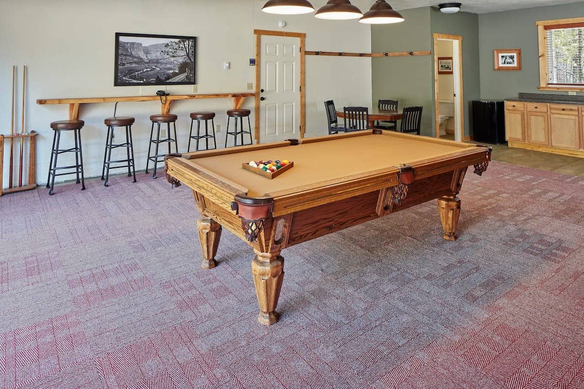 Pool table under hanging lamps with bar seating along the wall