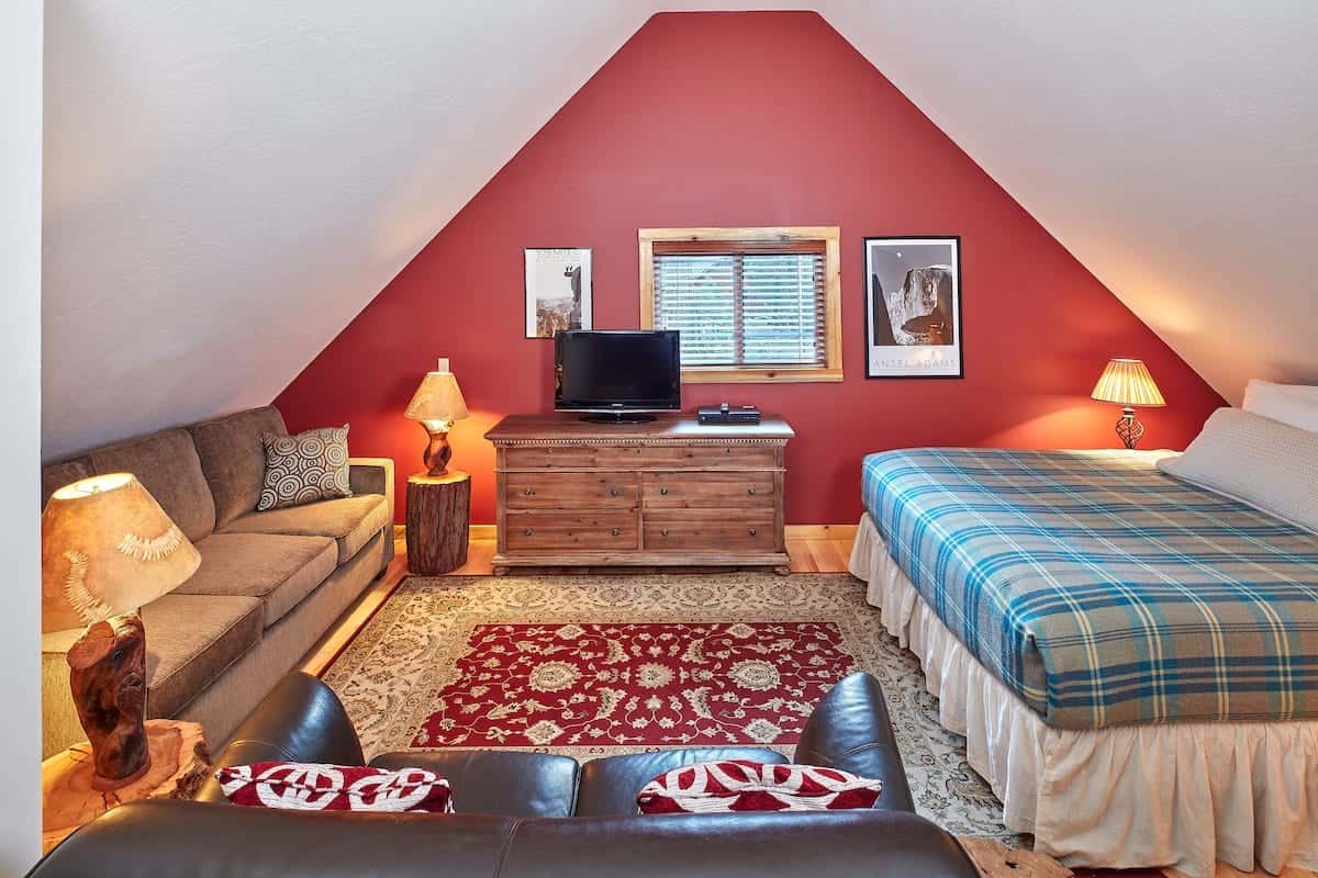 Studio loft under a vaulted ceiling with a red accent wall, a bed with a plaid quilt, a sofa, and a TV