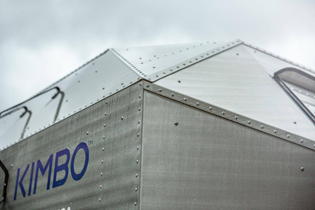Close-up of the Kimbo 6 faceted aluminum shell, rows of hand rivets, blue KIMBO wordmark, overcast sky