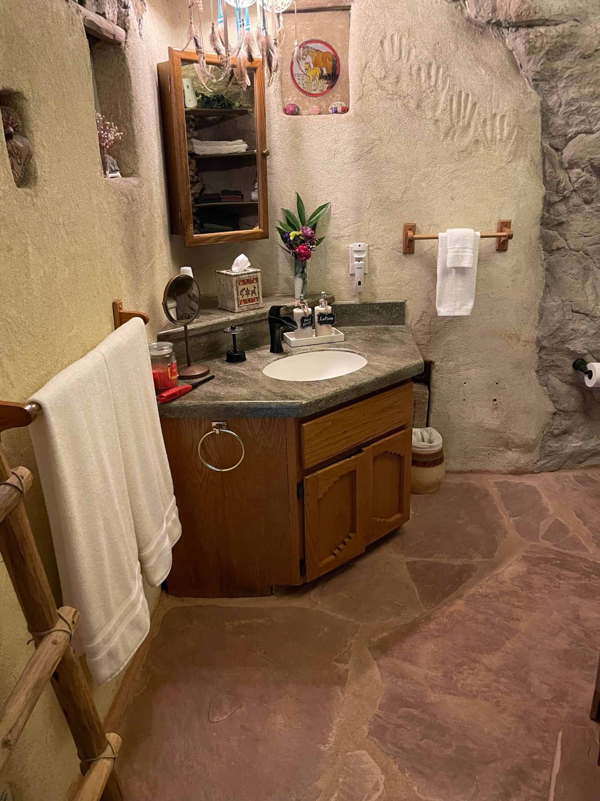 Bathroom vanity on flagstone with mixed rock walls, carved-wood cabinet, oval sink