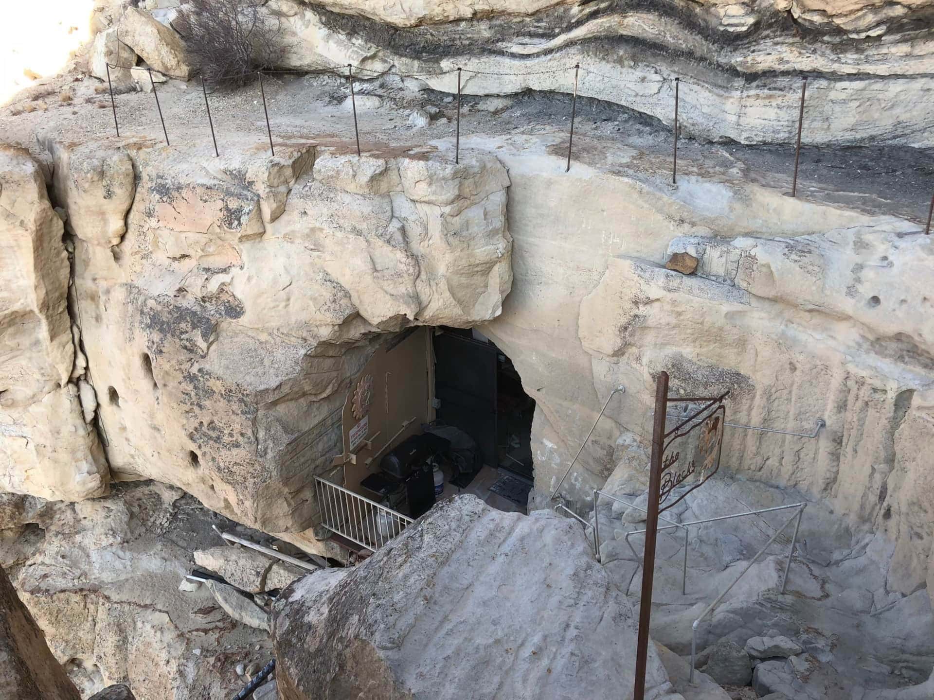 Main entrance at the cave mouth: arched doorway in sandstone, metal rail, Kokopelli-style sign