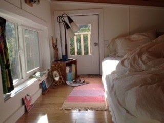 Sleeping loft with a low bed, a striped runner, and a white door with a window opening onto a small outdoor balcony