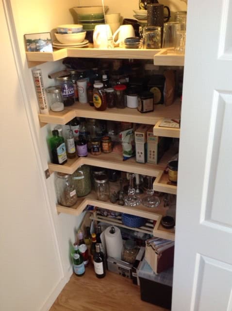 Custom wood pantry closet with stepped shelves packed with jars, dishes, and everyday supplies