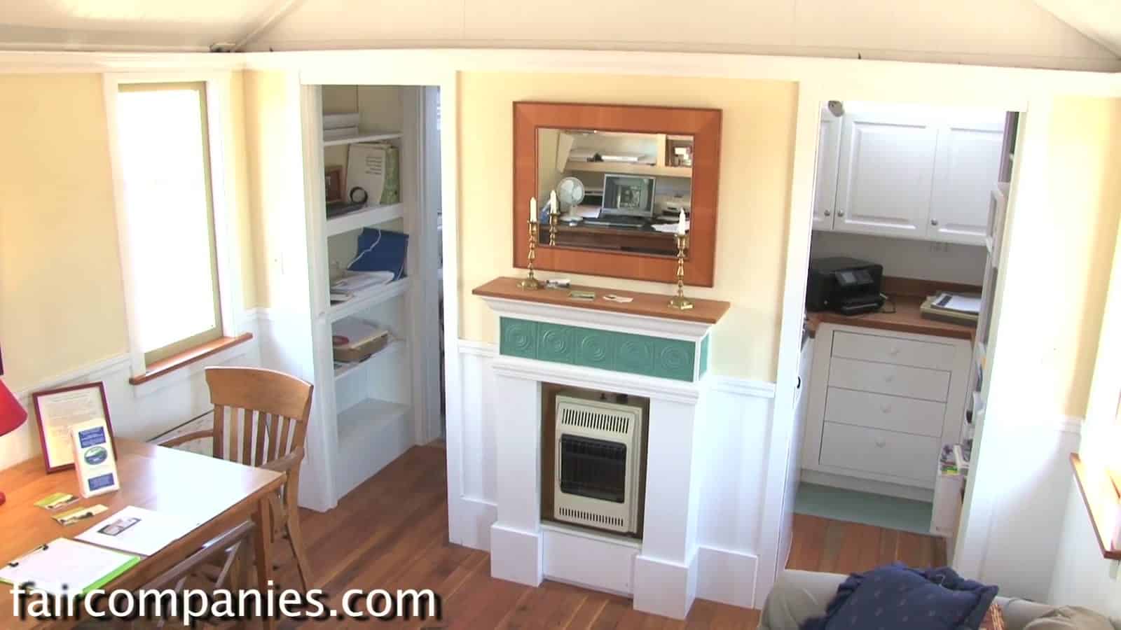 Interior of the 120 sq ft Little House on a Trailer with a white fireplace mantel, mirror, built-in shelves and kitchenette