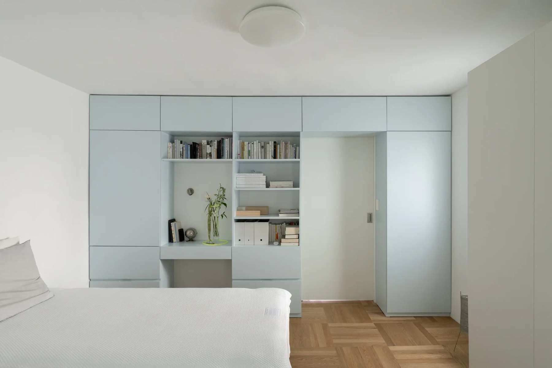 Bedroom with a full-height wall of pale blue cabinets with open shelves and a small desk alcove