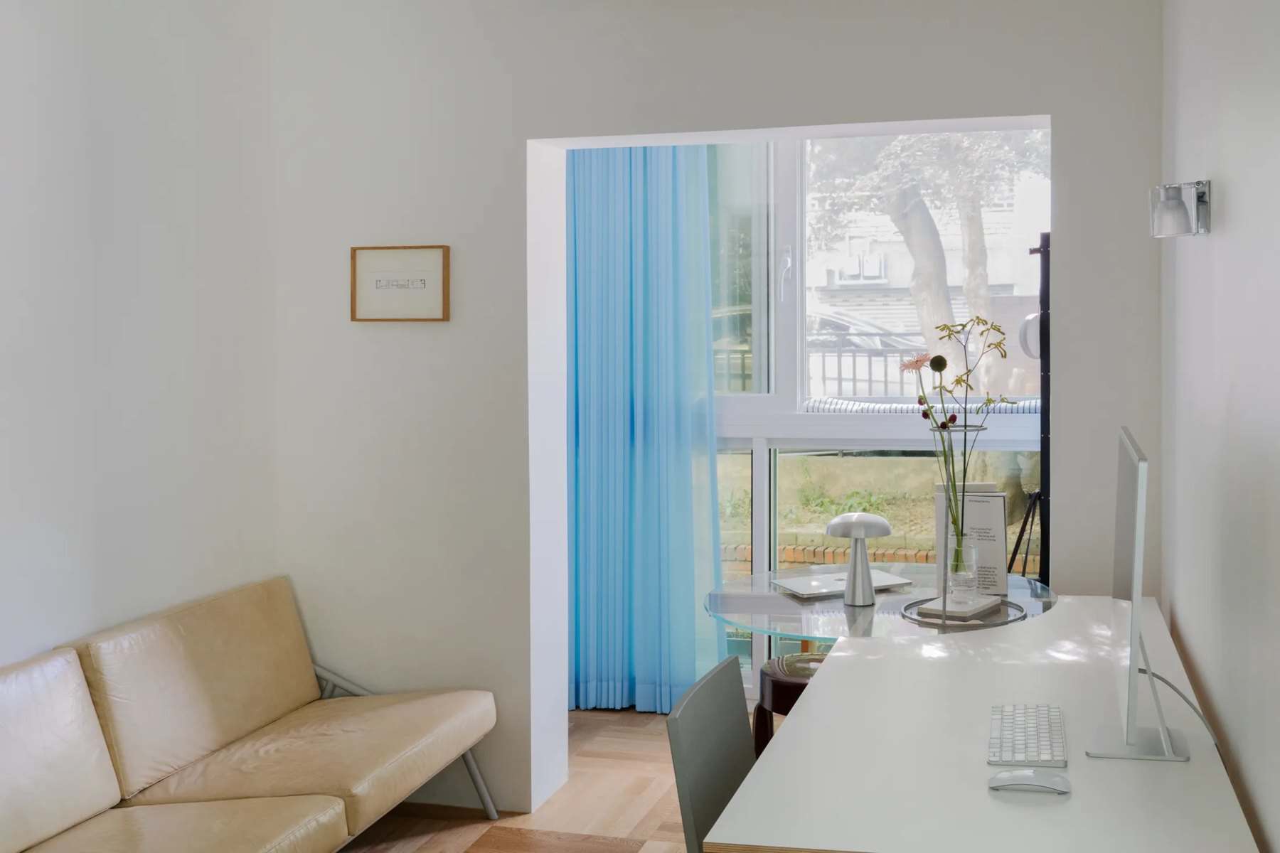 Enclosed balcony with a blue sheer curtain, a cream sofa, and a desk