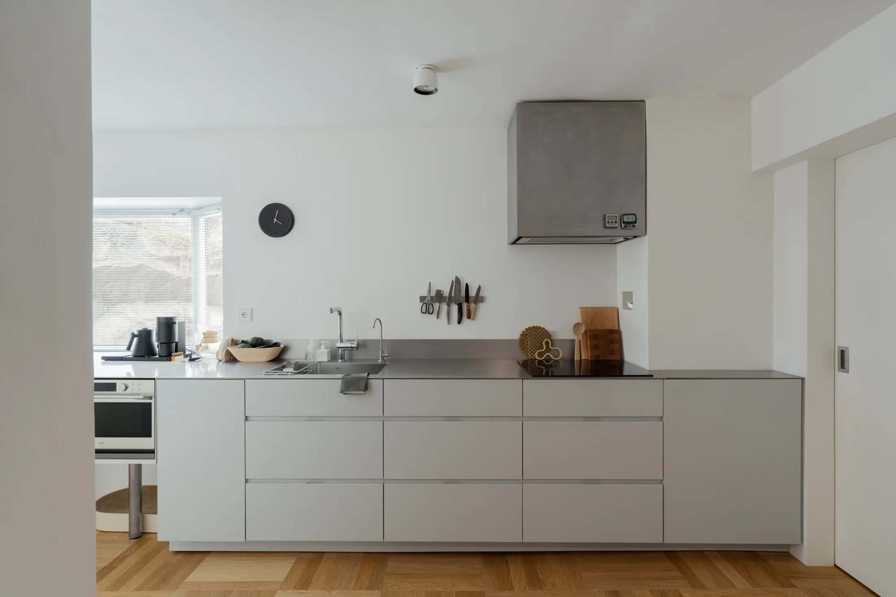 White kitchen with stainless counter, range hood, and wall oven on a parquet floor