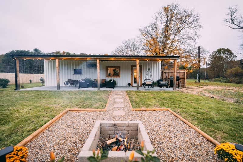 Covered patio of Luna Cottage: wood posts, string lights, two macrame swings, outdoor seating, grill at the far end, and a fire pit in the gravel
