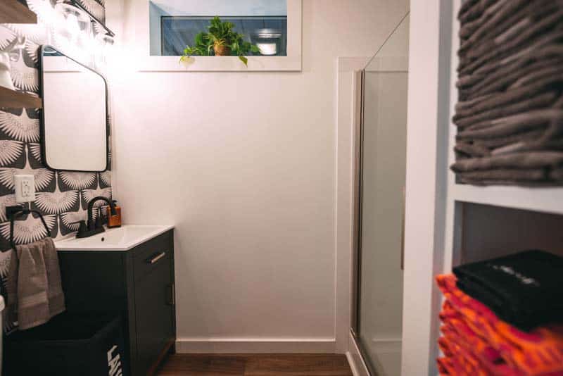 Bathroom of Luna Cottage: dark vanity with a black-framed mirror, patterned wallpaper, and a glass walk-in shower