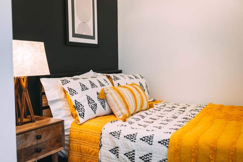 Bedroom of Luna Cottage: double bed with white and mustard bedding against a black accent wall, wood nightstand, and a lit lamp