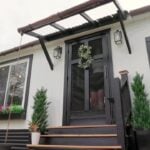 White board-and-batten 12x20 shed tiny house with black trim, screen door wreath, flower boxes, and wooden steps in Central Virginia