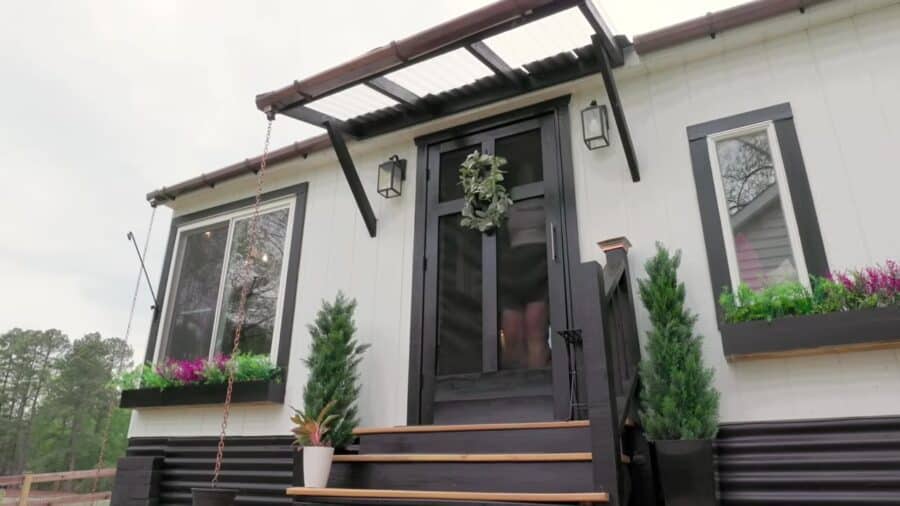 White board-and-batten 12x20 shed tiny house with black trim, screen door wreath, flower boxes, and wooden steps in Central Virginia