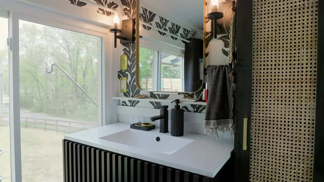 Bathroom vanity with black-and-white botanical wallpaper, white sink, matte-black faucet, and a large window to the yard