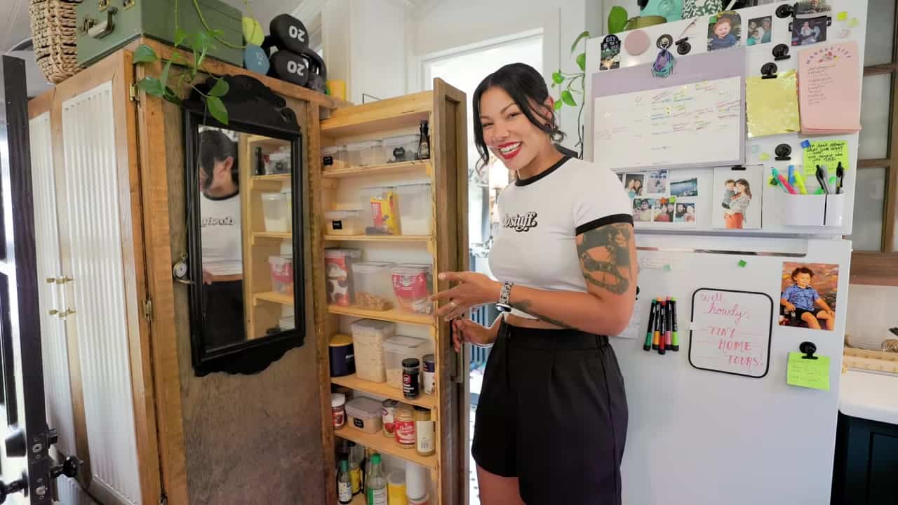 Custom wood closet with slatted doors and a pull-out pantry beside the white fridge in Margo Fairchild’s shed tiny house