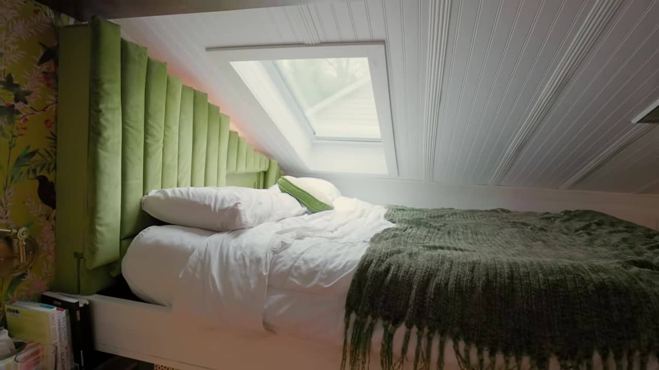 Queen loft bed under a skylight with an olive channel-tufted headboard fitted to the pitched beadboard ceiling