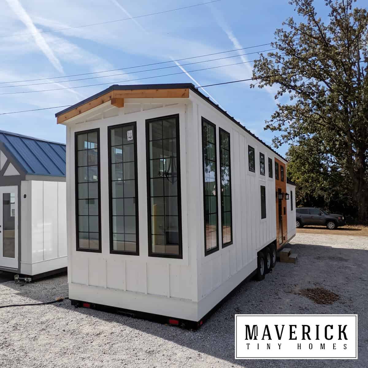 Maverick exterior: white board-and-batten, black-grid windows, wood accent side entry, triple-axle trailer