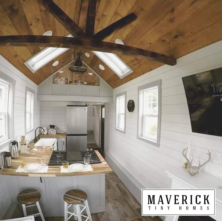 Maverick interior: pine ceiling with collar ties and skylights, butcher-block bar, farmhouse sink, loft rail over kitchen