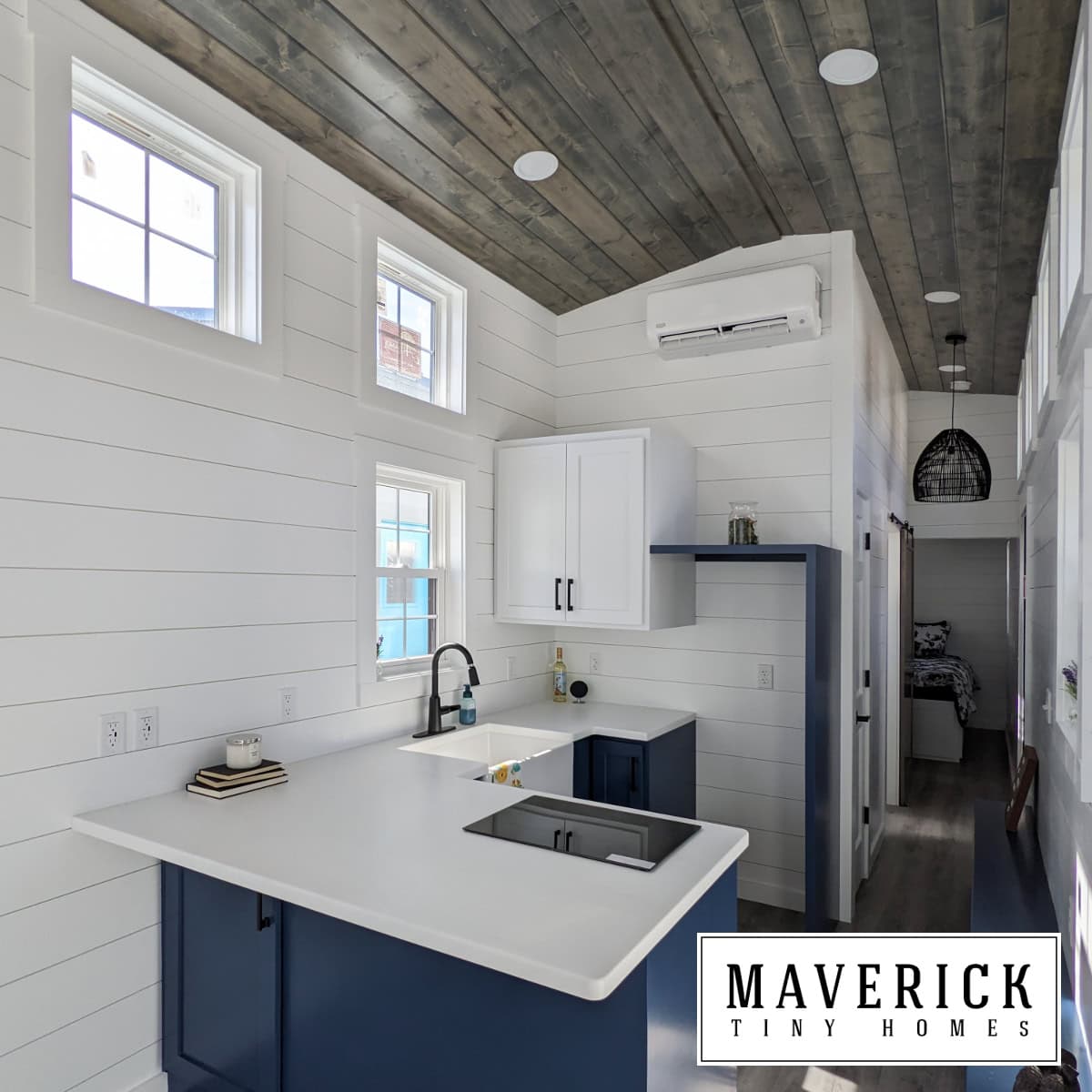 Maverick kitchen: navy lowers, white farmhouse sink, black cooktop on peninsula, open navy shelf, dark wood ceiling