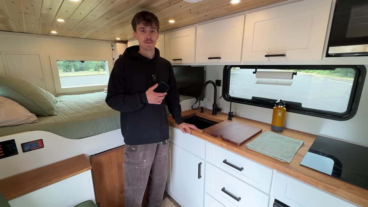 Galley kitchen with butcher-block counters and raised sage-green bed in Maxwell Peters off-grid tiny home van