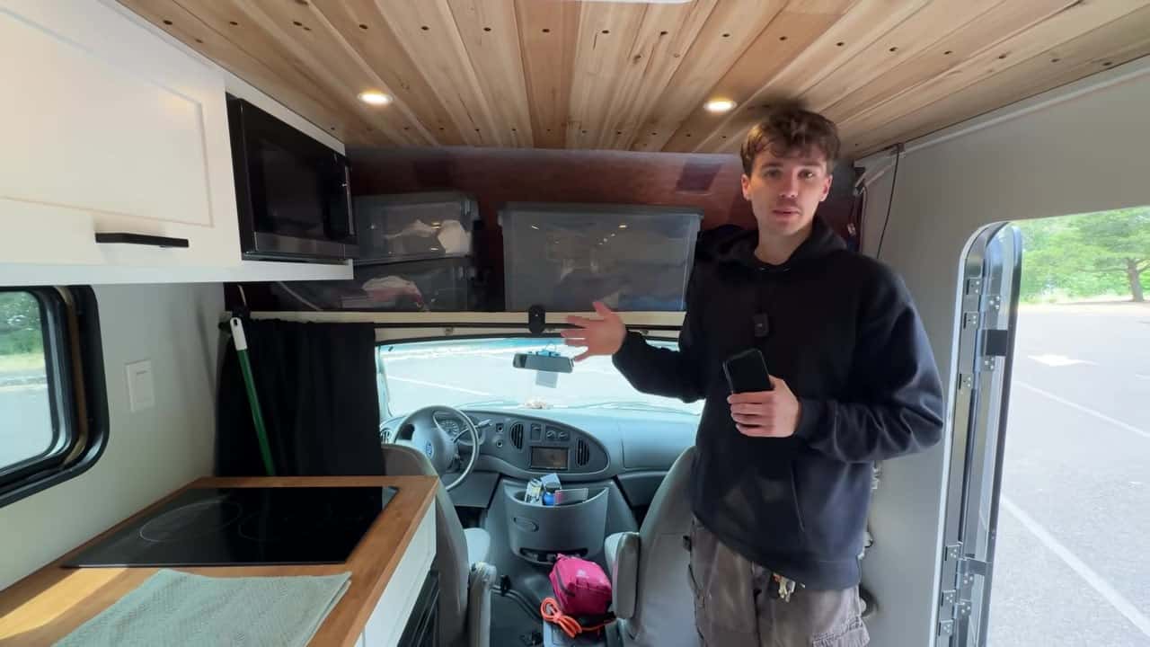 Interior of Maxwell Peters box van looking toward the cab with wood ceiling, induction cooktop, and over-cab storage