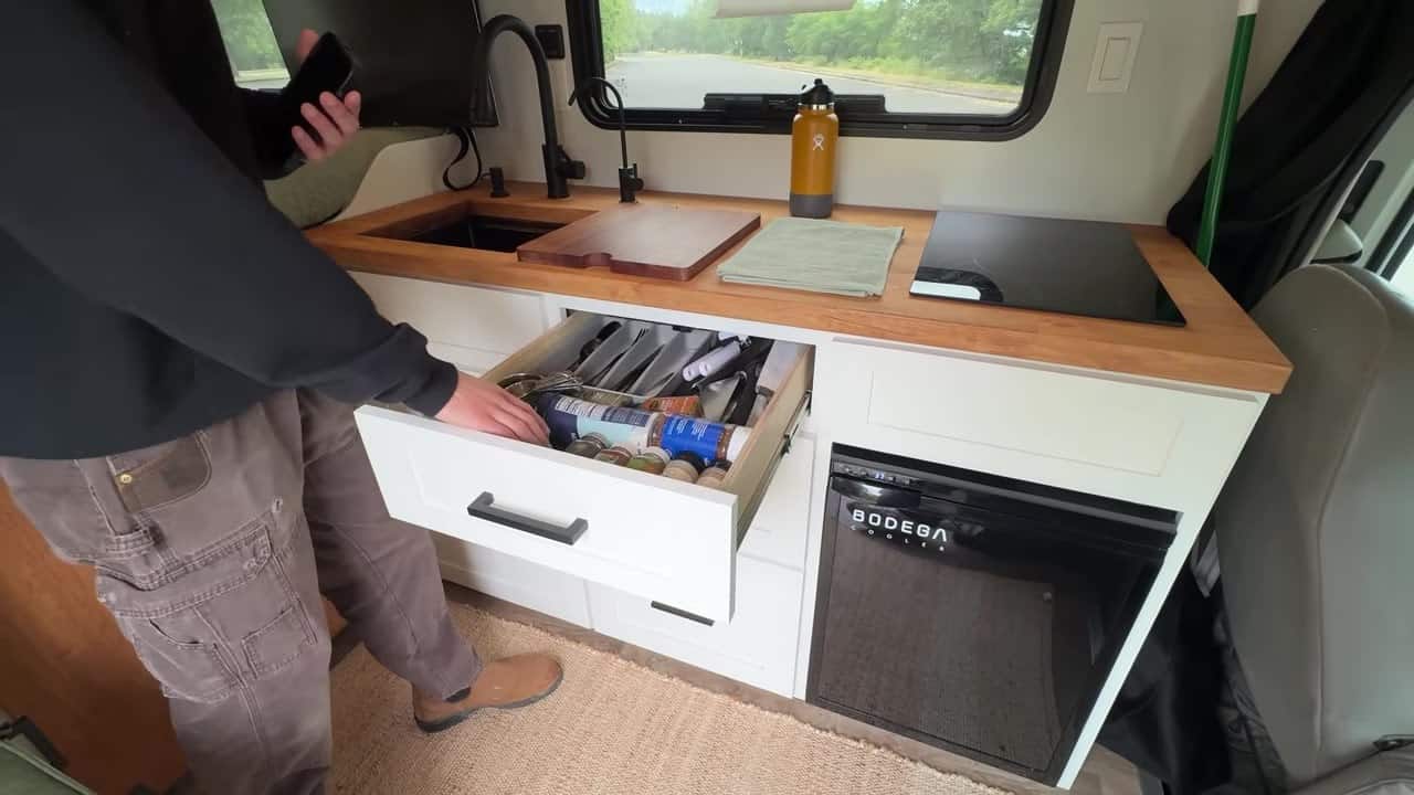 Kitchen drawer open beside Bodega cooler fridge under wooden countertop in Maxwell Peters van conversion