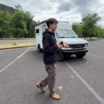 Maxwell Peters walking beside his white Ford E-350 moving van converted into an off-grid tiny home with rooftop solar