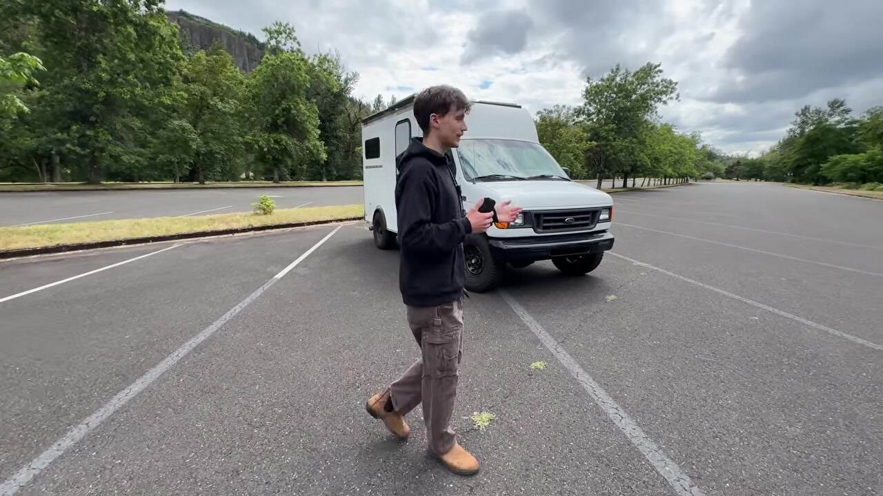 Maxwell Peters walking beside his white Ford E-350 moving van converted into an off-grid tiny home with rooftop solar