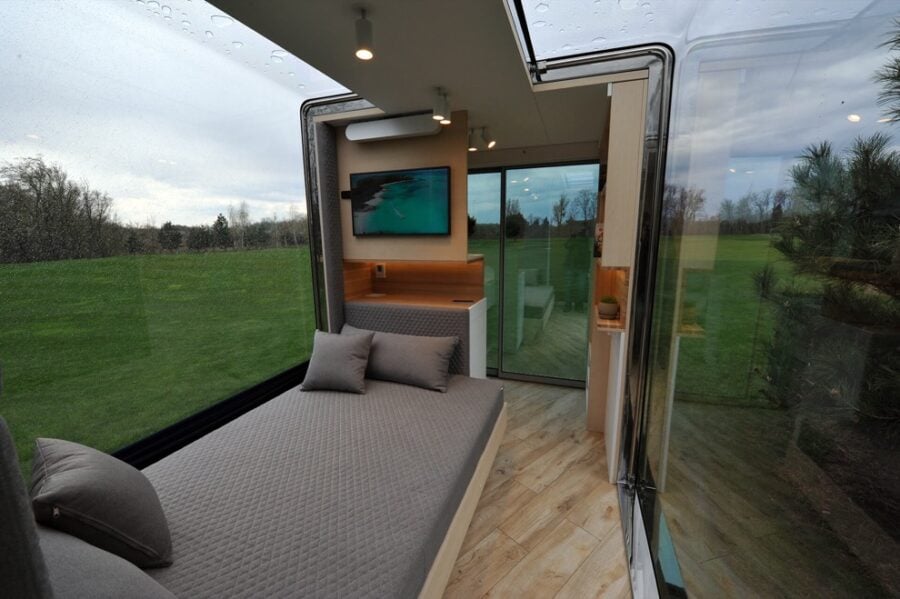 Bright interior of a tiny house with large windows and cozy sleeping area.