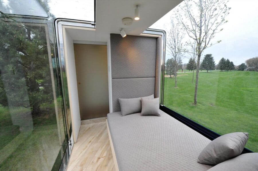 Compact tiny house interior with large windows and cozy bed.