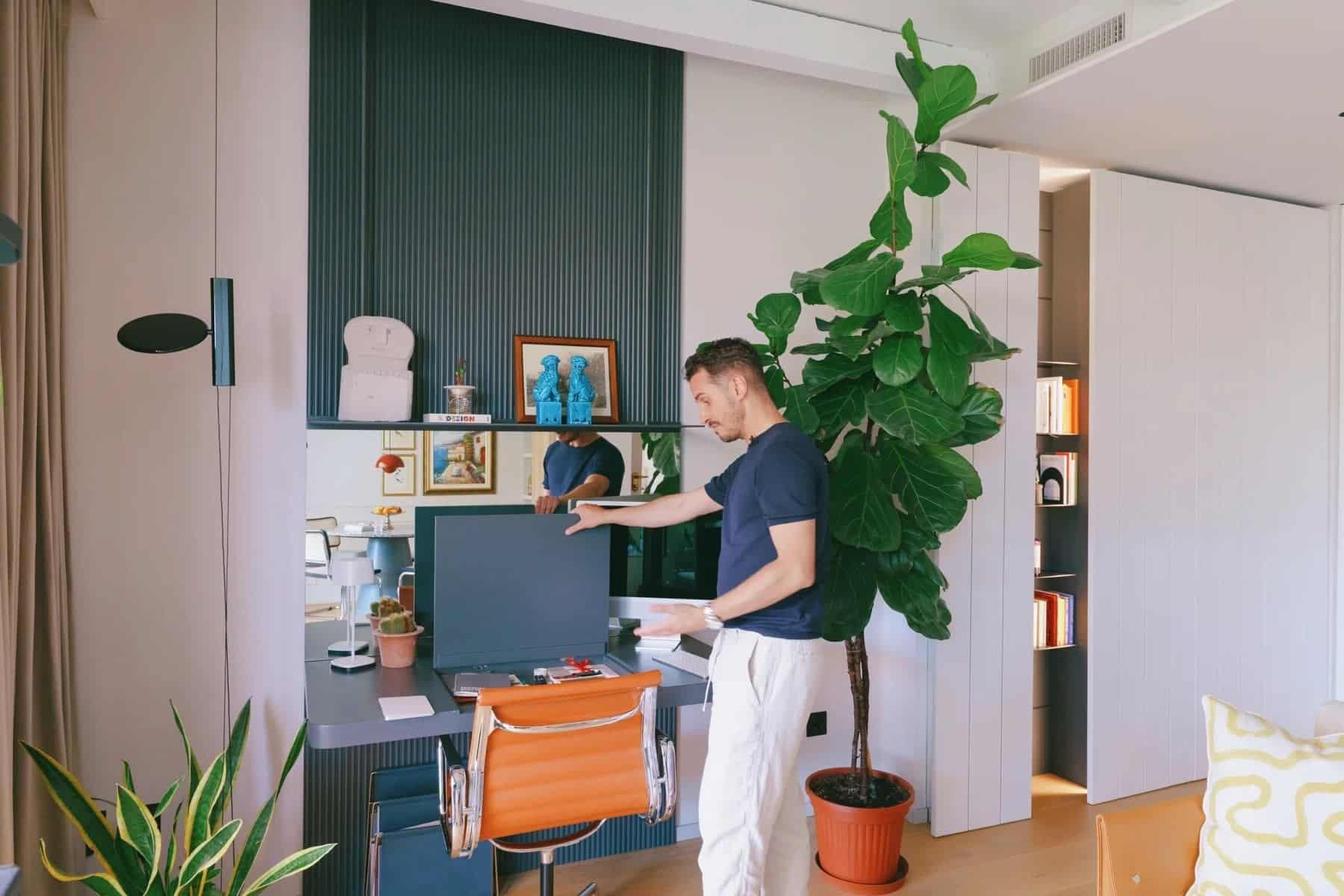 Simone at his custom dark wood desk in the living room, with plants and wall shelves