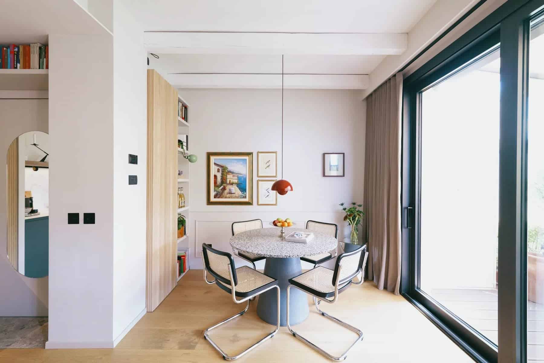 Round terrazzo dining table with cane chairs beside floor-to-ceiling windows