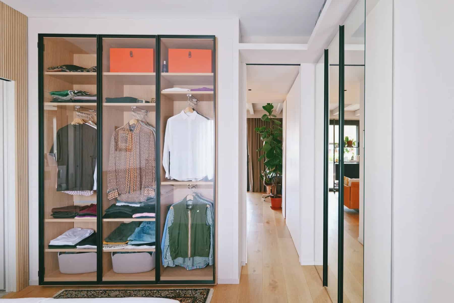 Glass-front wardrobe with clothes hanging on front-facing rails