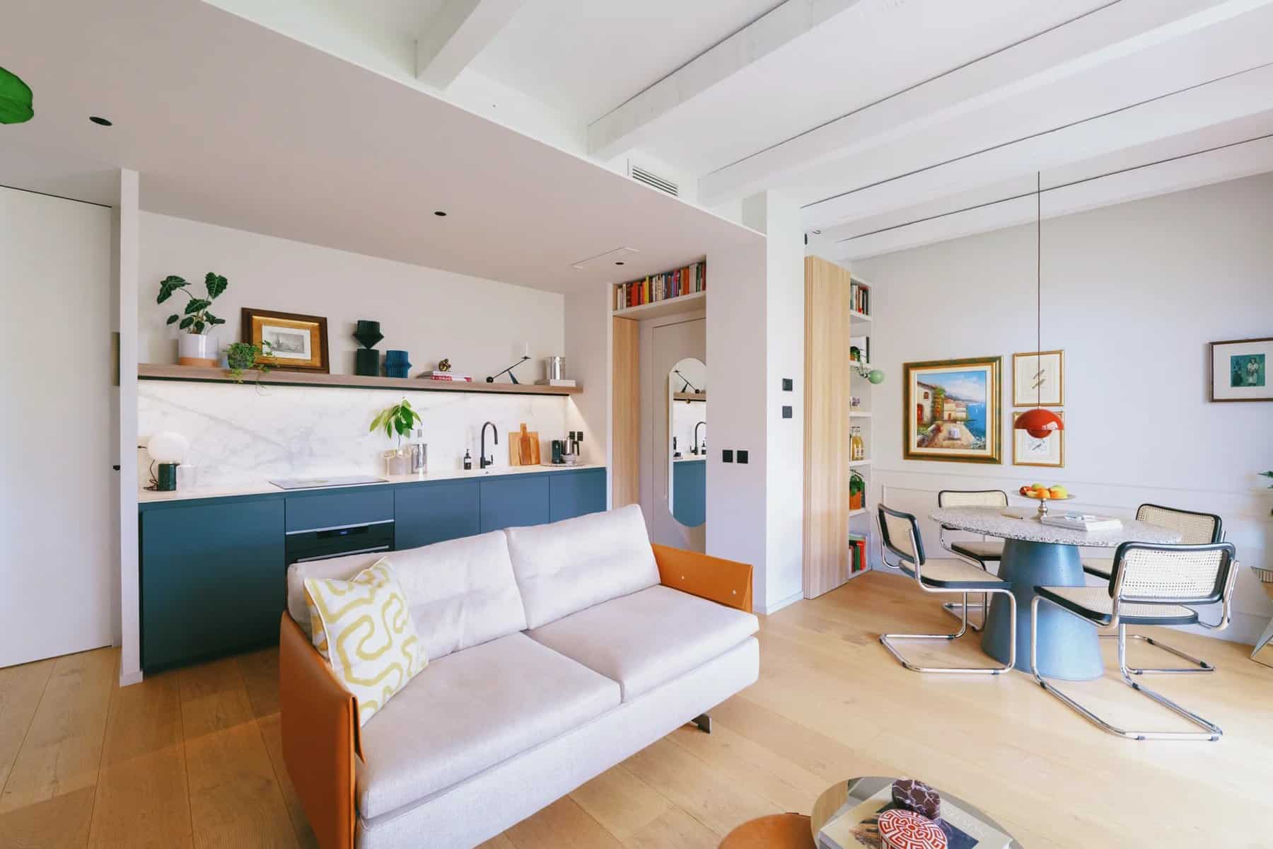 Simone Mongini's Milan apartment: open kitchen with dark blue cabinets, white sofa, and round dining table