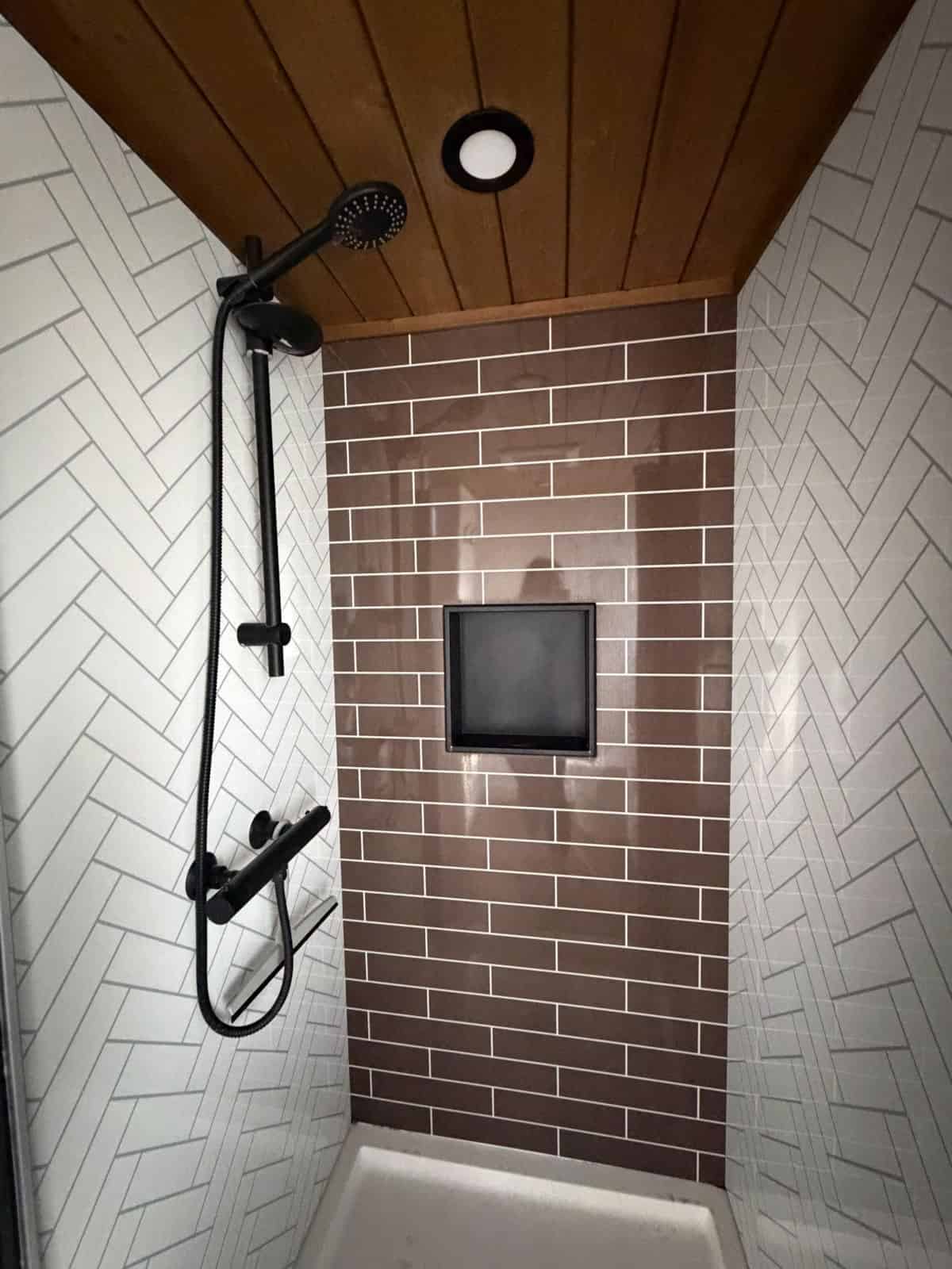 Tiled shower with herringbone tile, dark accent wall and black rain shower fixture