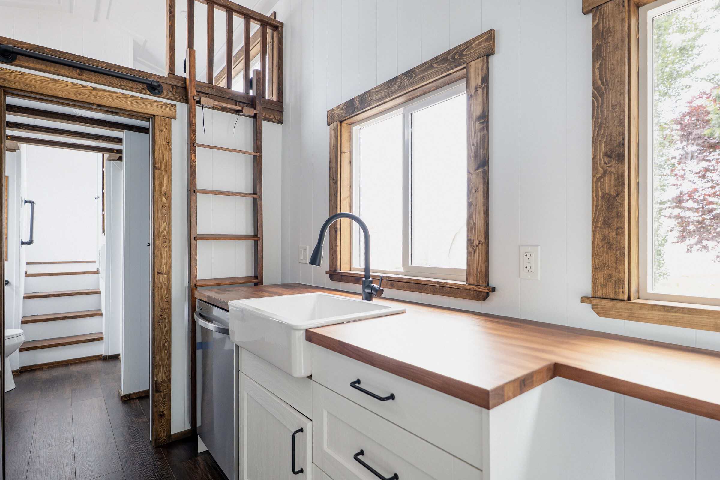 Arctic galley: butcher-block counter, ceramic apron sink, black faucet, white cabinetry, loft ladder and dark loft rail above