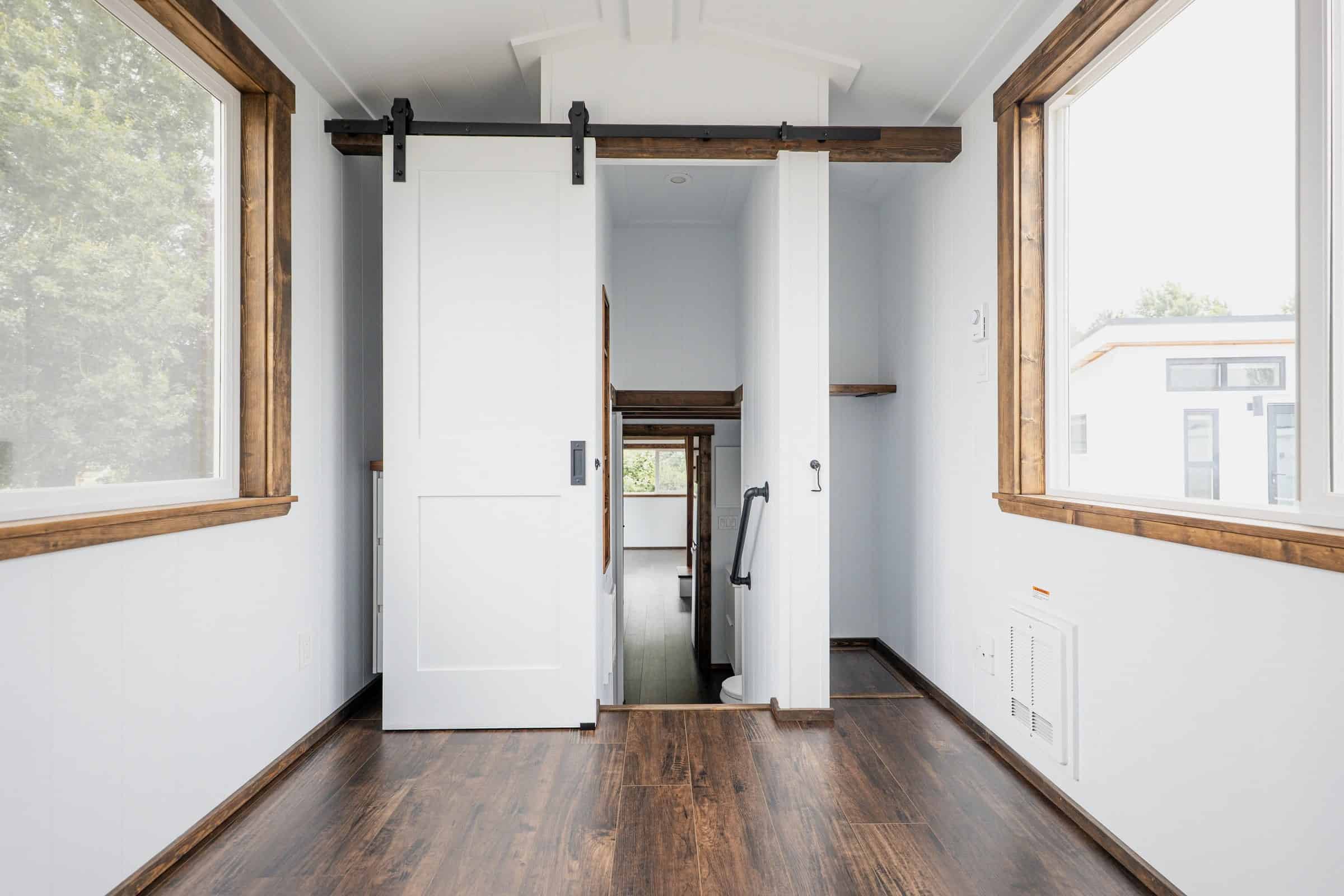 Gooseneck bedroom of the Arctic: white walls, dark wood floor and window trim, white sliding barn door open to the hall, standing-height room