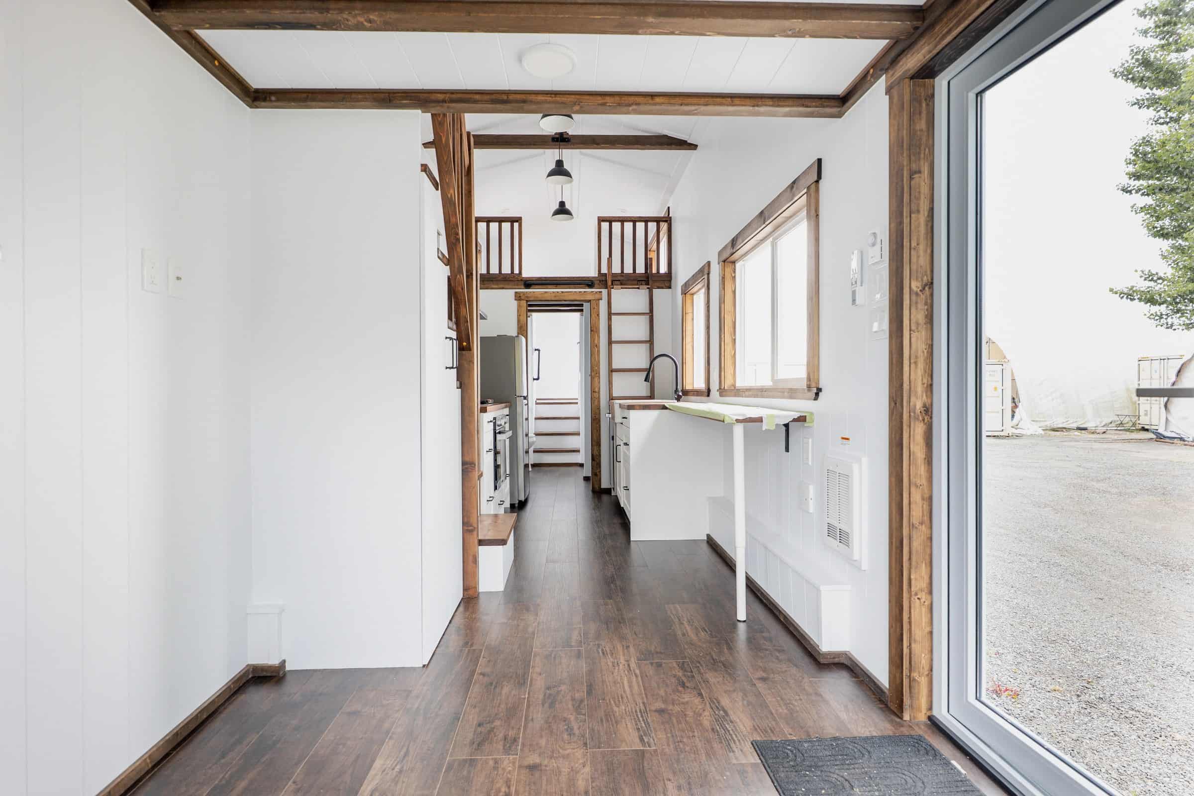 Living corridor of the Arctic: white shiplap, dark beams and railings, French door, stairs, loft ladder, galley beyond