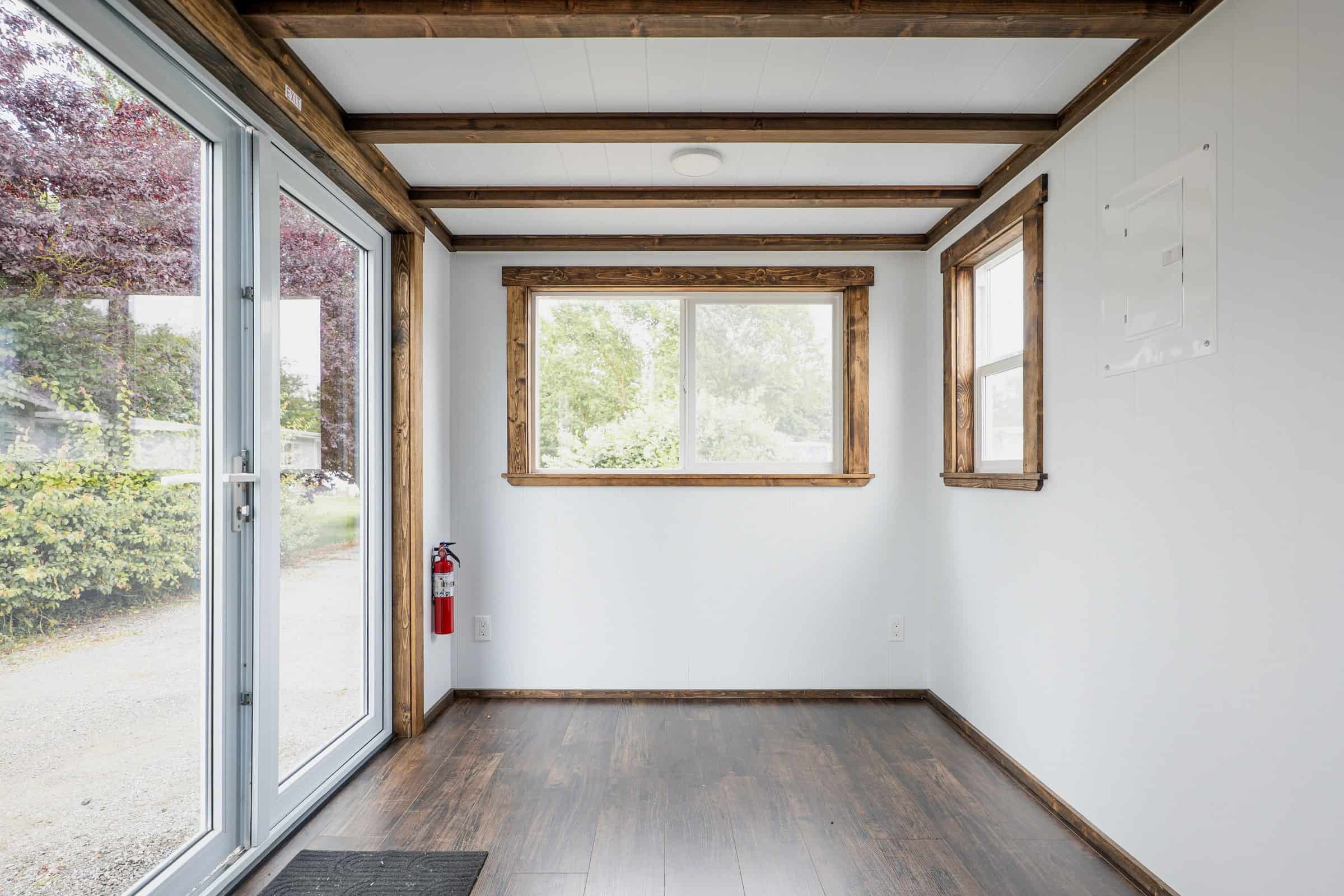 Empty living room of the Arctic: white walls and ceiling, dark wood floor and beams, white French doors, sliding window on the end wall