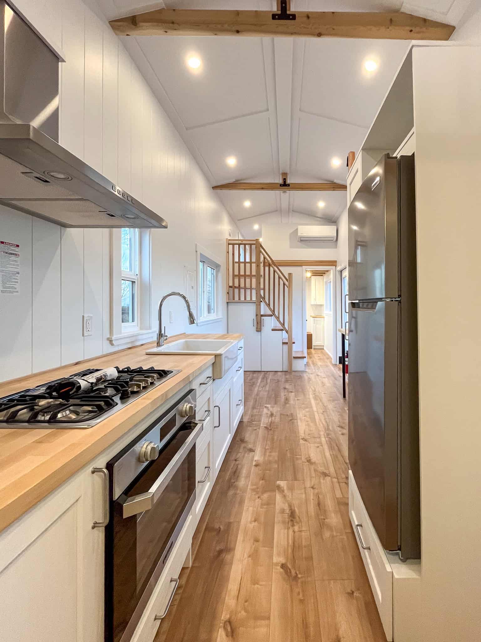Galley of the Loft Ruby: butcher-block counter, white apron sink, four-burner cooktop and oven, stainless fridge, wood storage stairs, vaulted ceiling with wood beams