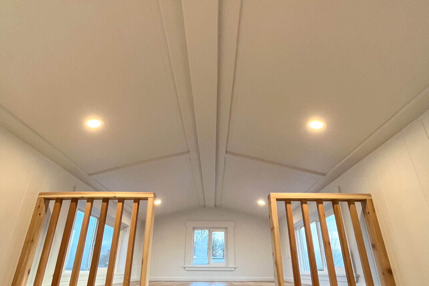 Vaulted paneled ceiling between two loft railings of square wood slats, side windows and a square window at the far gable