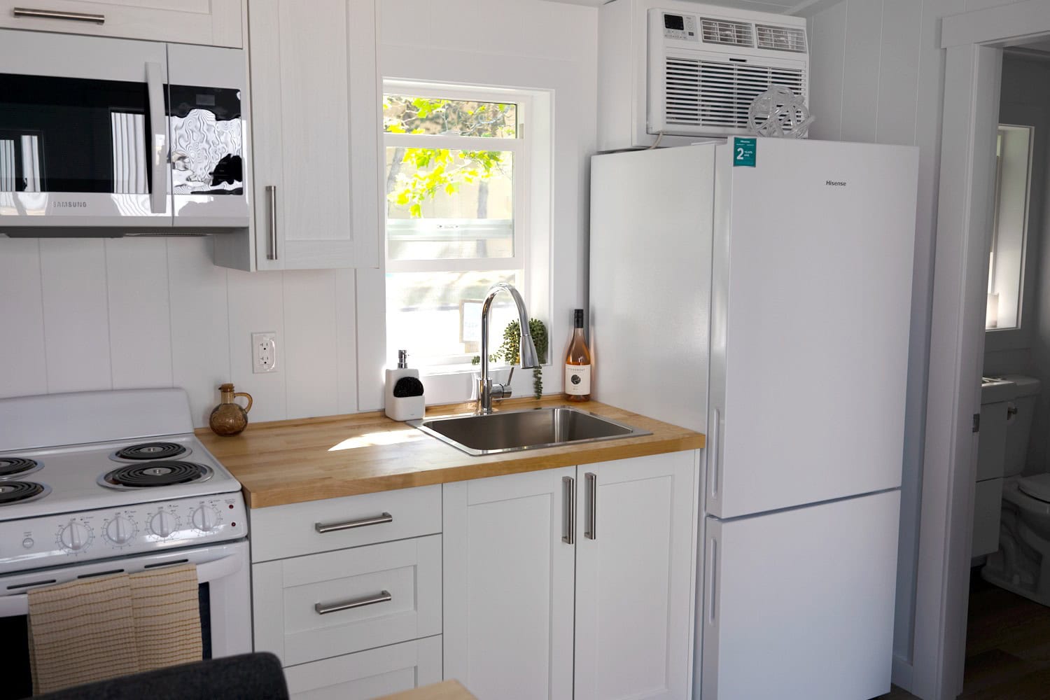 Jason kitchen: white shaker cabinets, butcher-block veneer, stainless sink with chrome pull-down faucet, 28-inch fridge, 24-inch slide-in range, wall air-conditioning unit